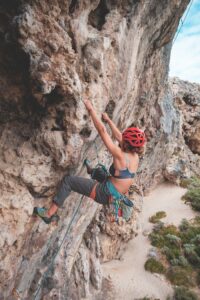Side view of anonymous female with rope in helmet climbing on stony terrain