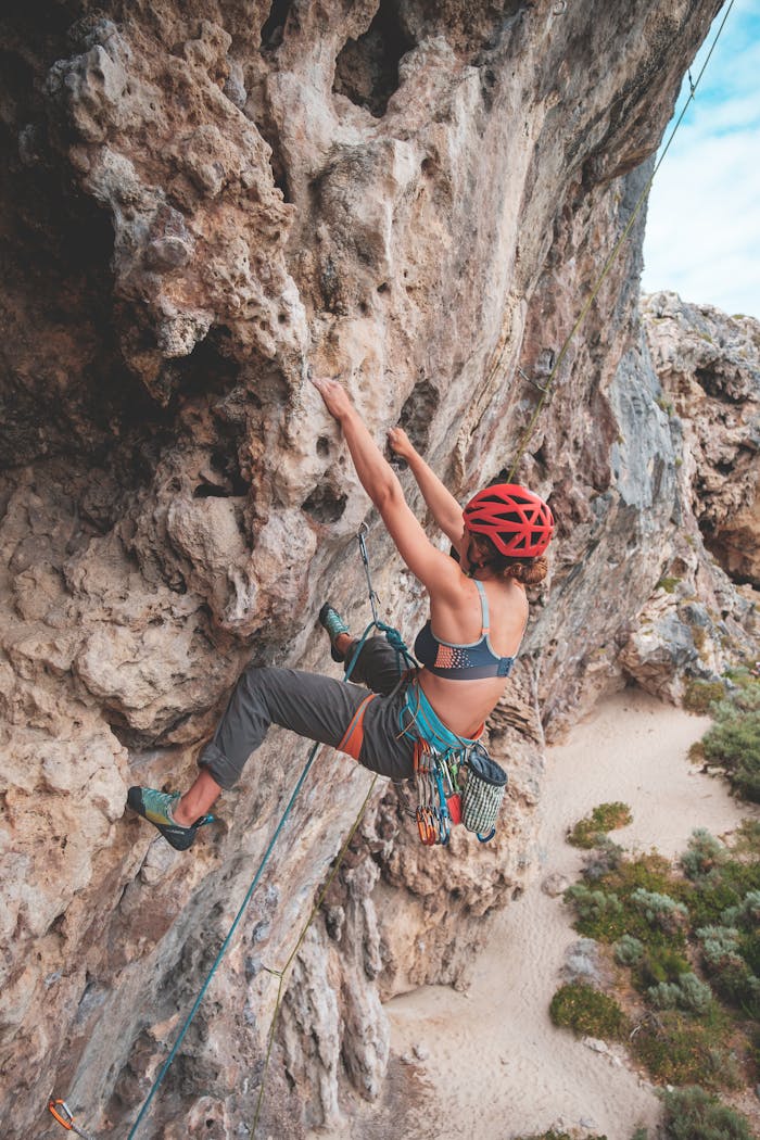Side view of anonymous female with rope in helmet climbing on stony terrain